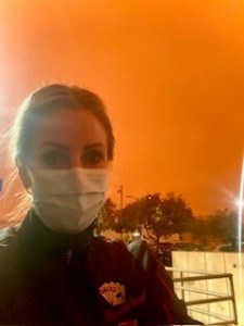 Woman with surgical mask stands at instrument install with dark orange sky in background